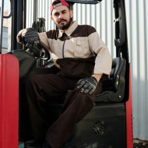 Male forklift operator in industrial uniform sitting on a forklift outdoors.