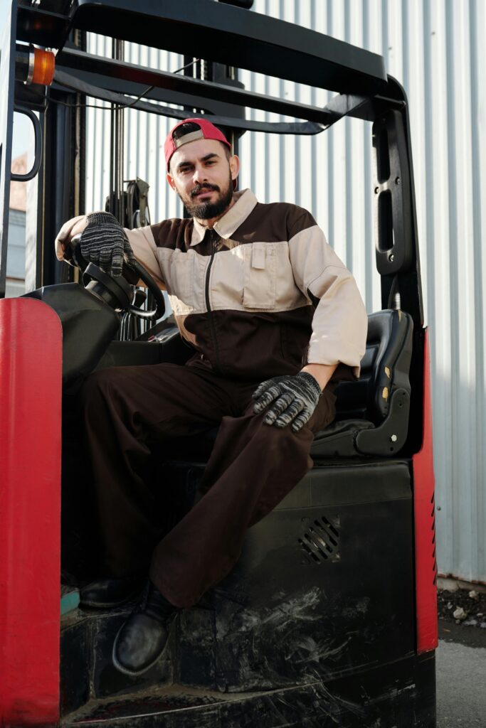 Male forklift operator in industrial uniform sitting on a forklift outdoors.