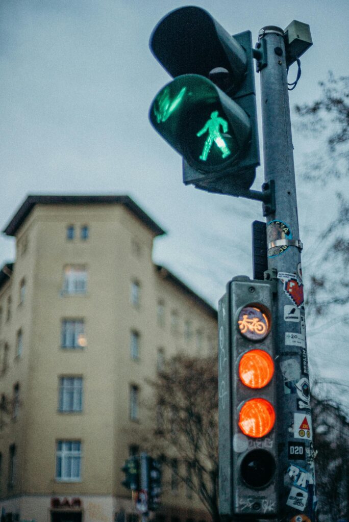 Traffic light with green pedestrian signal in urban setting, featuring building and cyclist symbol.