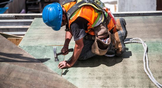 A skilled construction worker in protective gear hammering a rooftop panel.